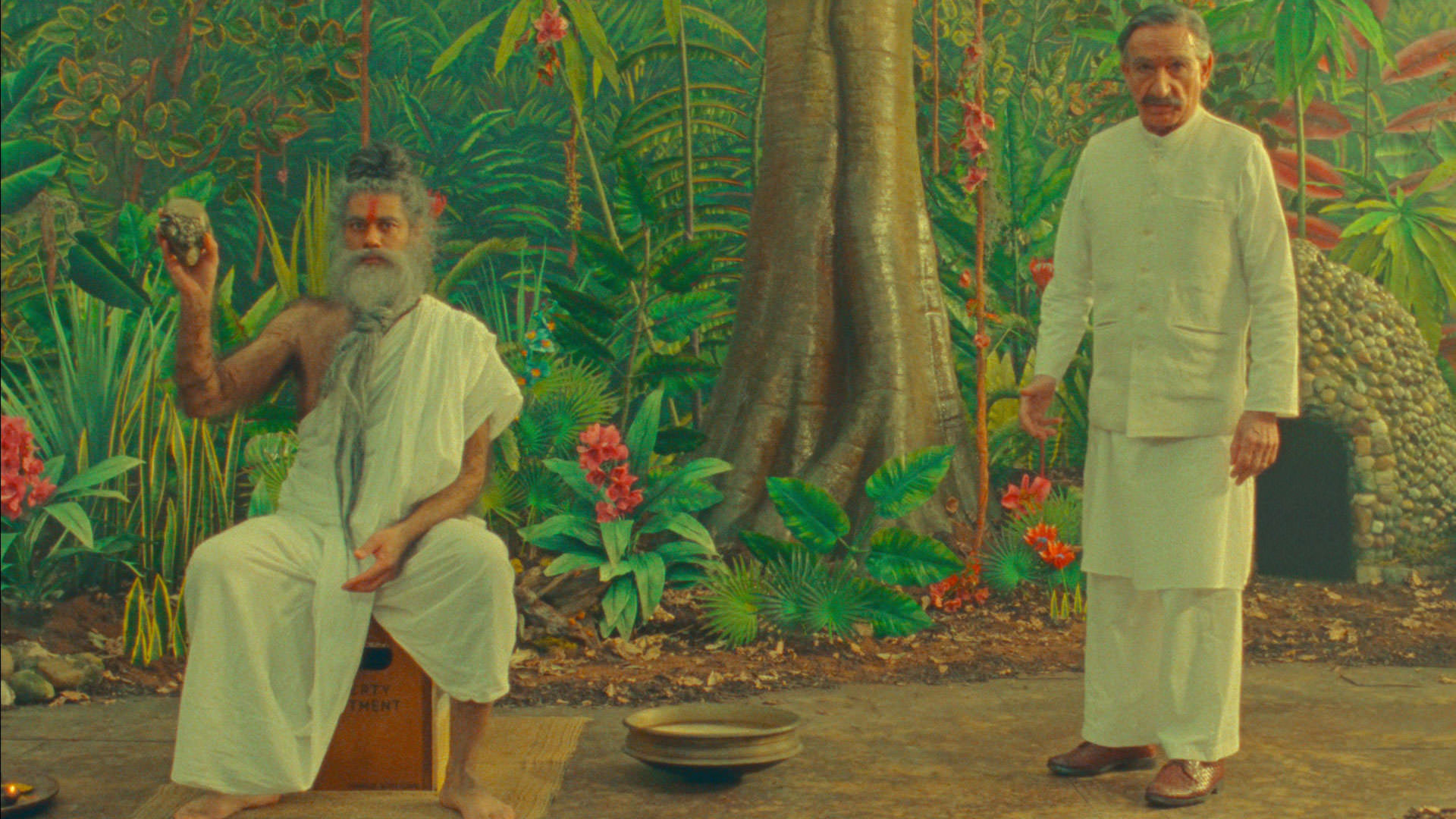 بن کینگزلی با لباس سفید هندی در کنار ریچارد آیوادی در نقش یک مرتاض که سنگی را در دست دارد جلوی دکوری از یک جنگل در نمایی از فیلم کوتاه داستان شگفت‌انگیز هنری شوگر به کارگردانی وس اندرسون